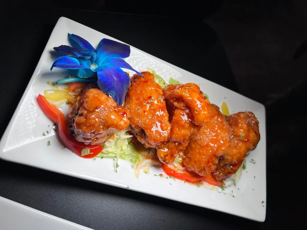 Sweet chili chicken wings on a white plate with a blue orchid.