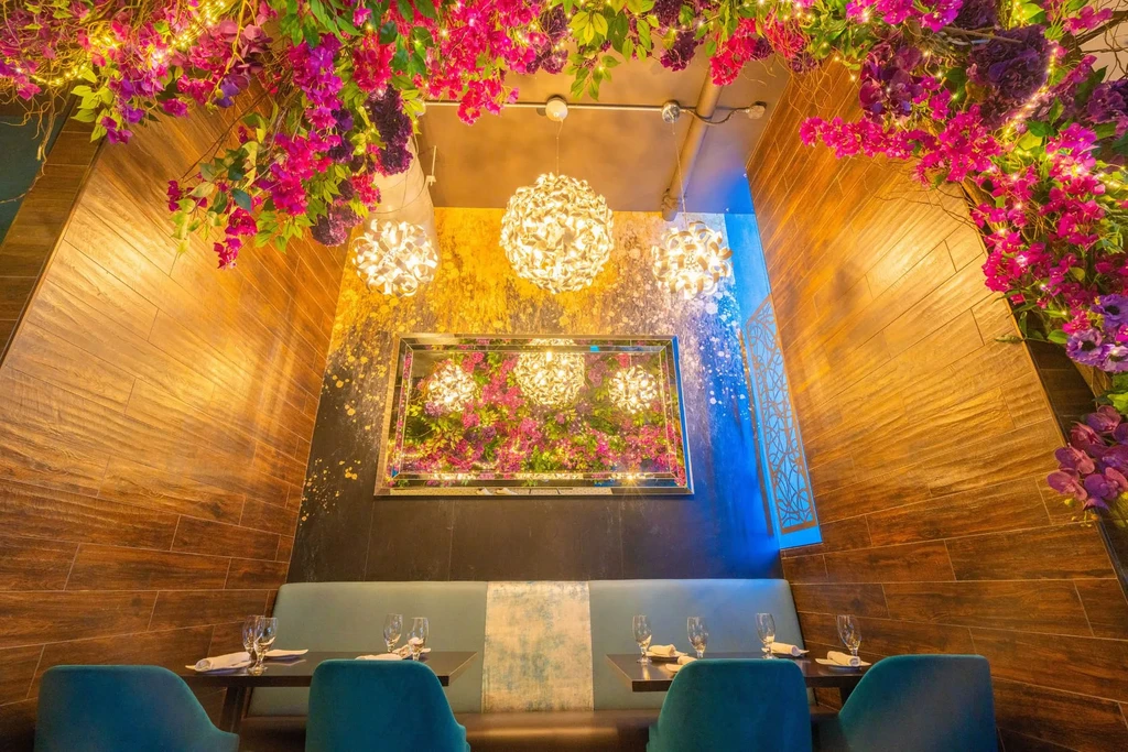 Restaurant interior with purple and pink flowers, ornate lighting, and teal seating.