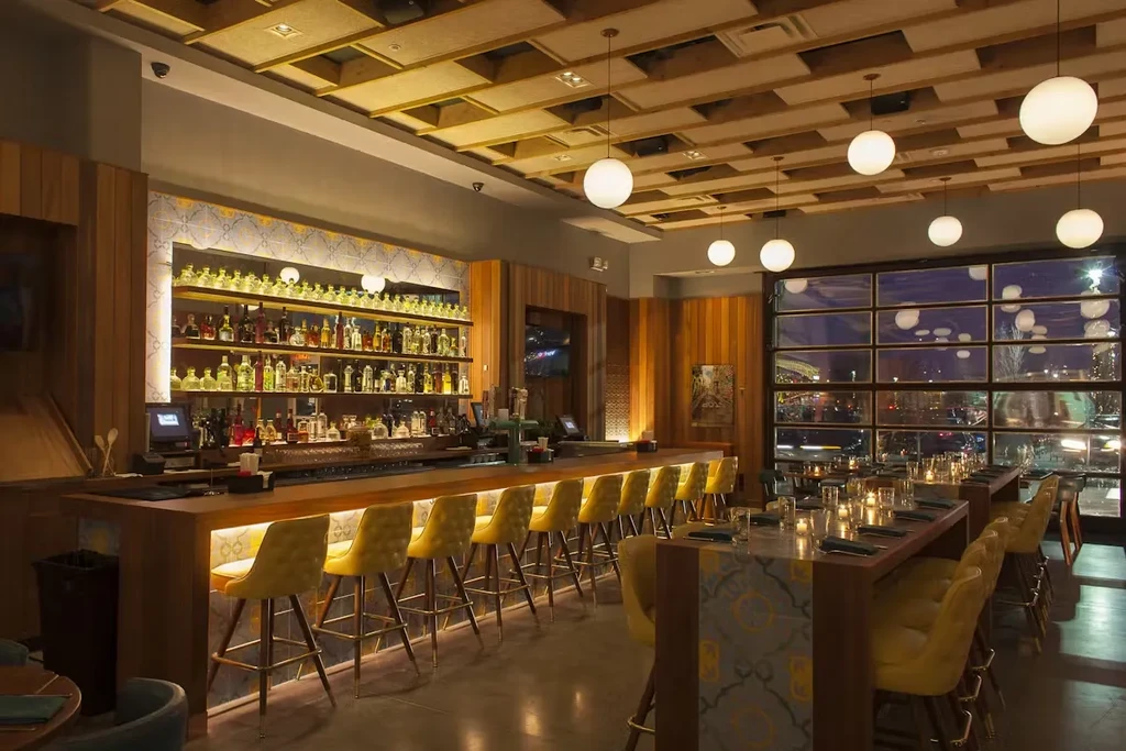 A modern restaurant interior with a long bar and bright yellow stools.