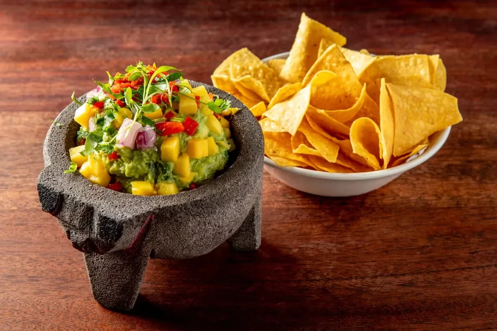 Guacamole in a molcajete with mango, red peppers, and tortilla chips.