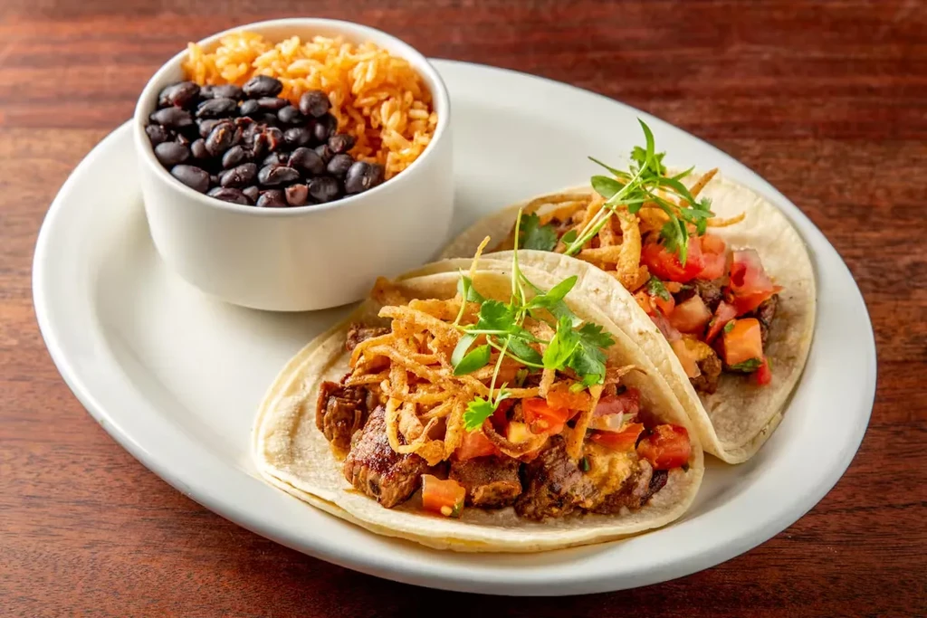 Two tacos, rice, and black beans on a white plate.