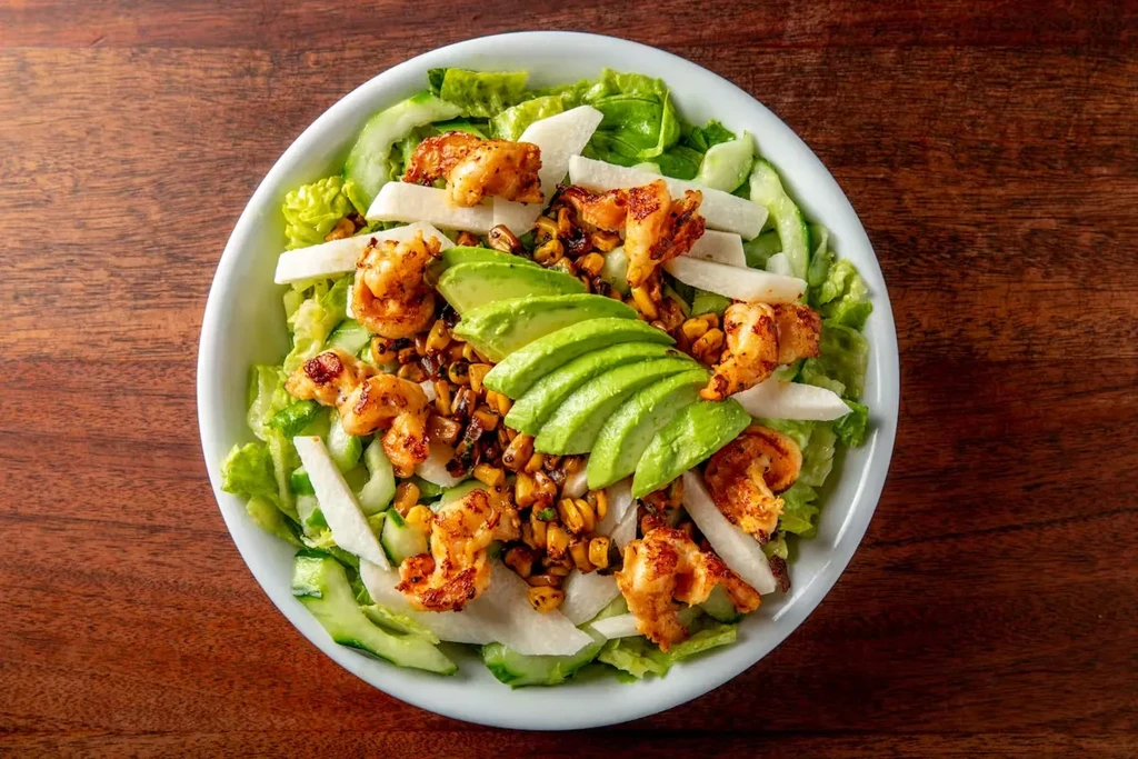 Overhead view of a shrimp, avocado, and vegetable salad in a white bowl.