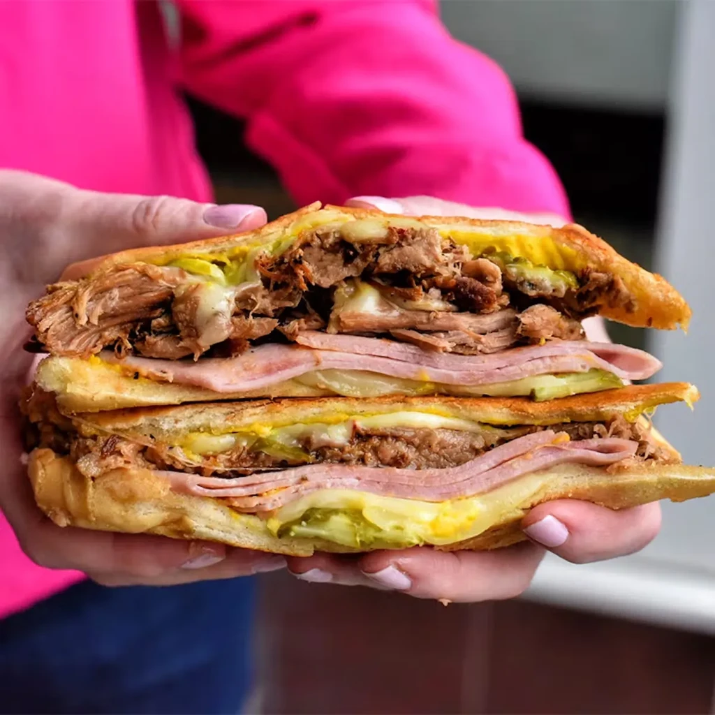A person holding a large, sliced Cuban sandwich with visible fillings.