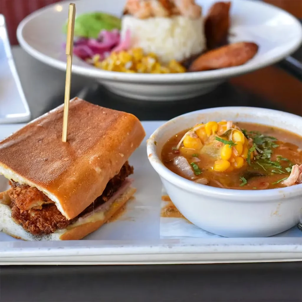 Cuban sandwich, soup with corn on the cob, and a blurry plate of food.