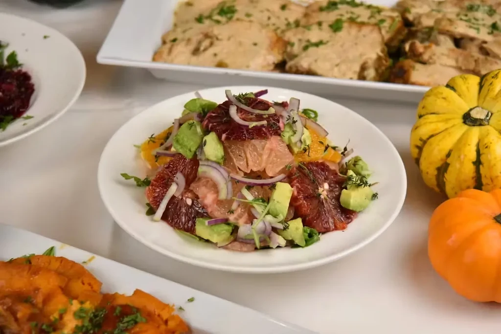 A citrus and avocado salad with red onion and thyme on a white plate.