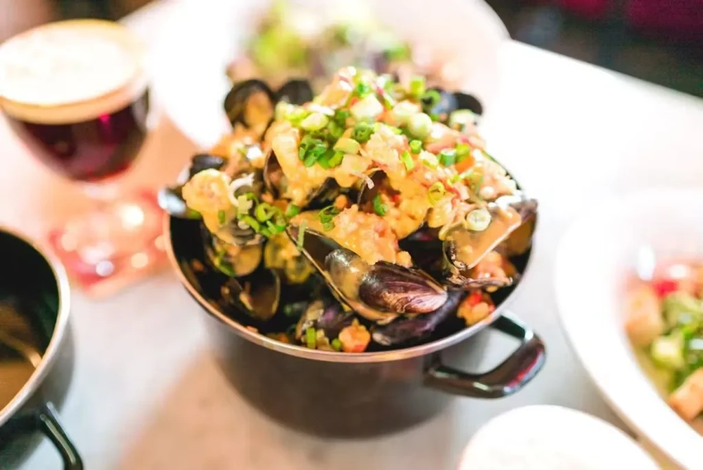 A black pot of mussels in sauce, topped with chopped chives.