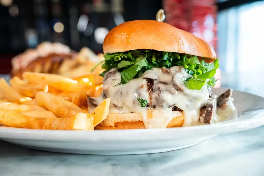 A burger with mushroom sauce and greens on a bun with fries.