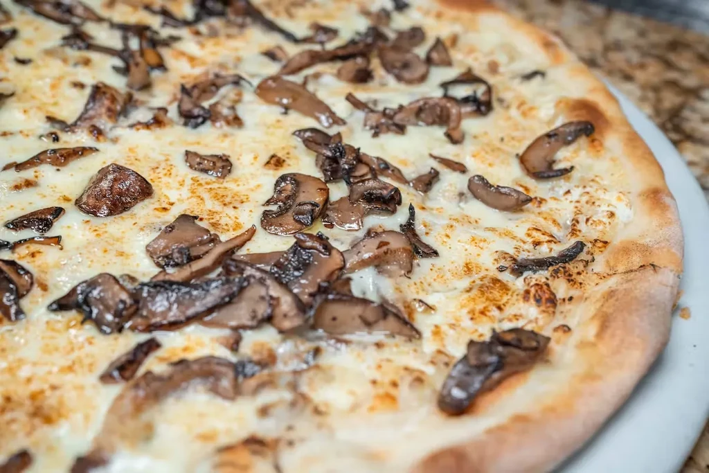 Close-up of a mushroom and cheese pizza on a white plate.