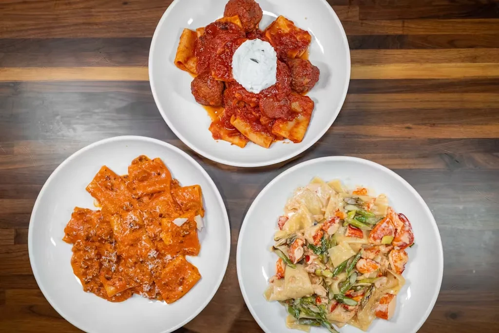 Three plates of pasta: Bolognese, lobster, and meatballs, on a wooden table.