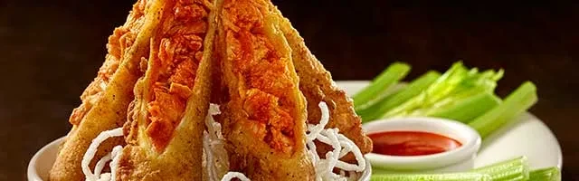 Golden fried, crunchy food with red sauce and celery sticks on a plate.