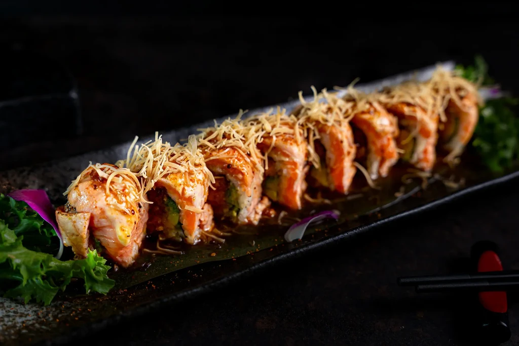 Close-up of a sushi roll topped with fried potato strings on a dark plate.