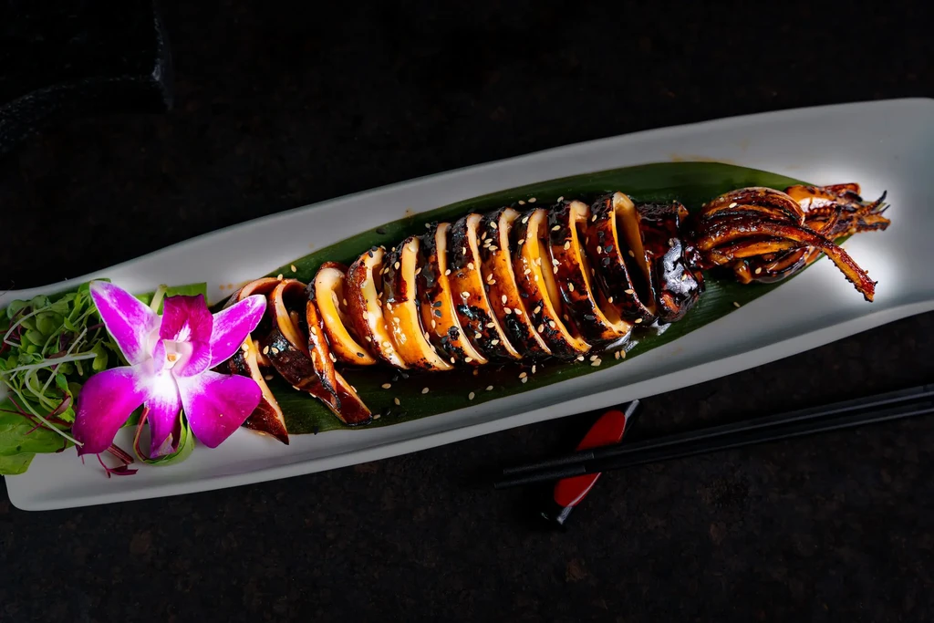 Grilled squid, sliced and drizzled with sauce, on a white platter.