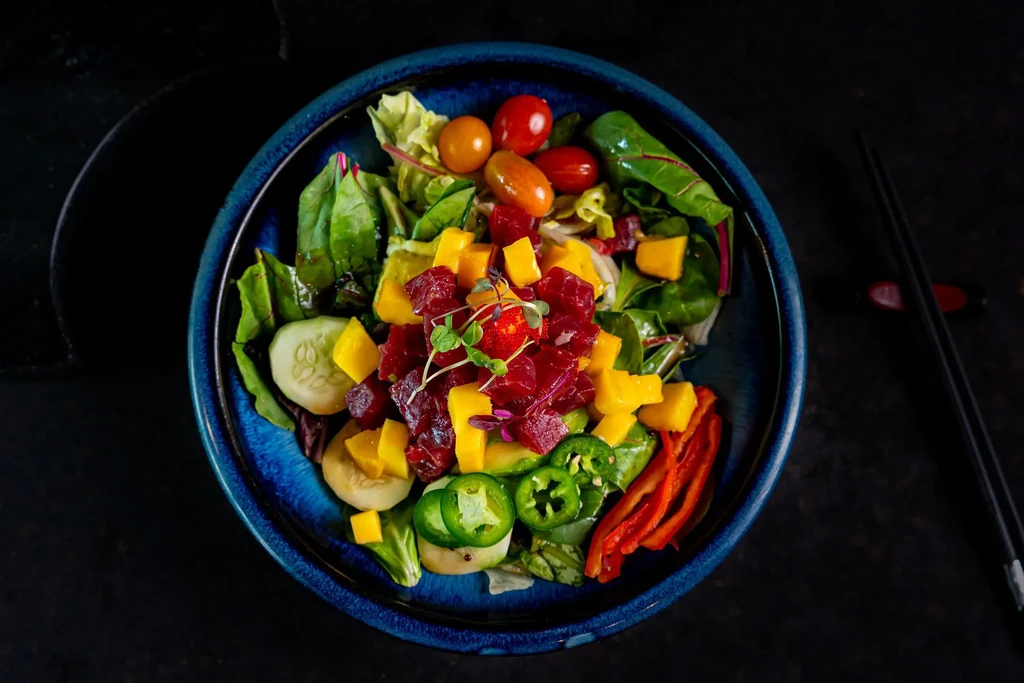 Overhead view of a colorful salad in a blue bowl with chopsticks.