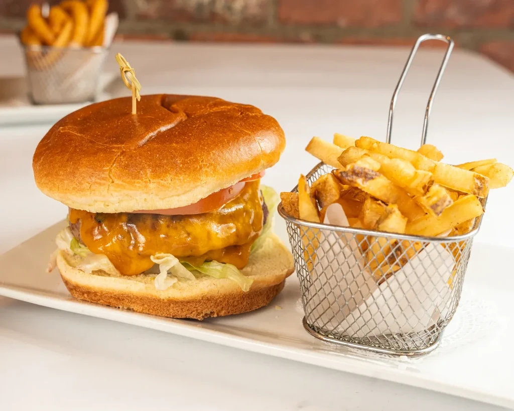A cheeseburger with fries in a basket on a white platter.