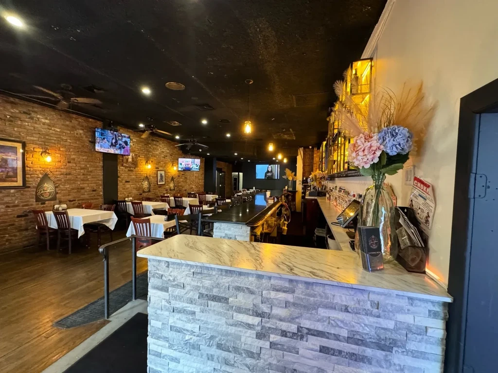 Empty restaurant interior with brick walls, black ceiling, and bar area.