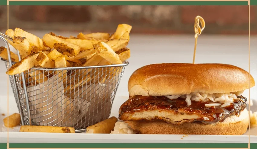 A barbecue chicken sandwich with coleslaw and a basket of fries.