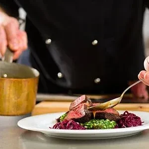 Chef drizzles sauce over perfectly cooked deer meat, red cabbage, and green puree.