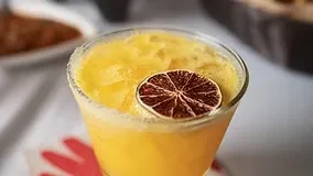 A close-up of a frosty orange drink with a dried lime garnish.