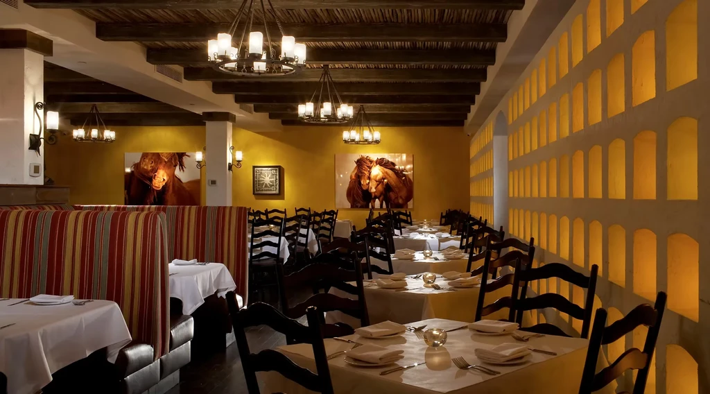 A restaurant with two horse paintings, chandeliers, and arched wall niches.
