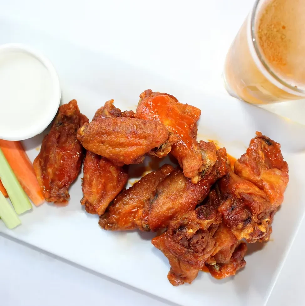 A plate of buffalo wings with dip, celery, carrots, and a drink.