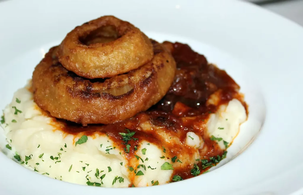 Mashed potatoes topped with gravy and two crispy onion rings.