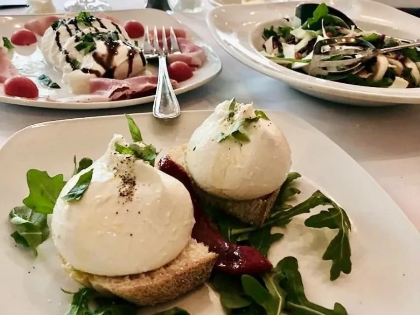 Two burrata cheese dishes, one with prosciutto, on a restaurant table.