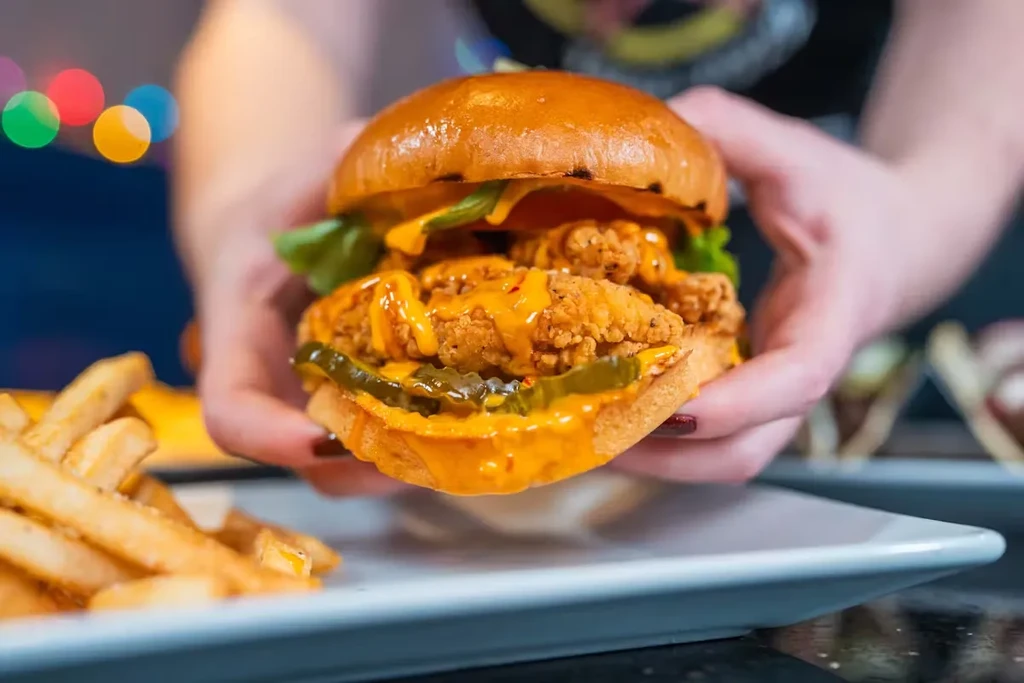 Hands holding a fried chicken sandwich with sauce, pickles, and fries.