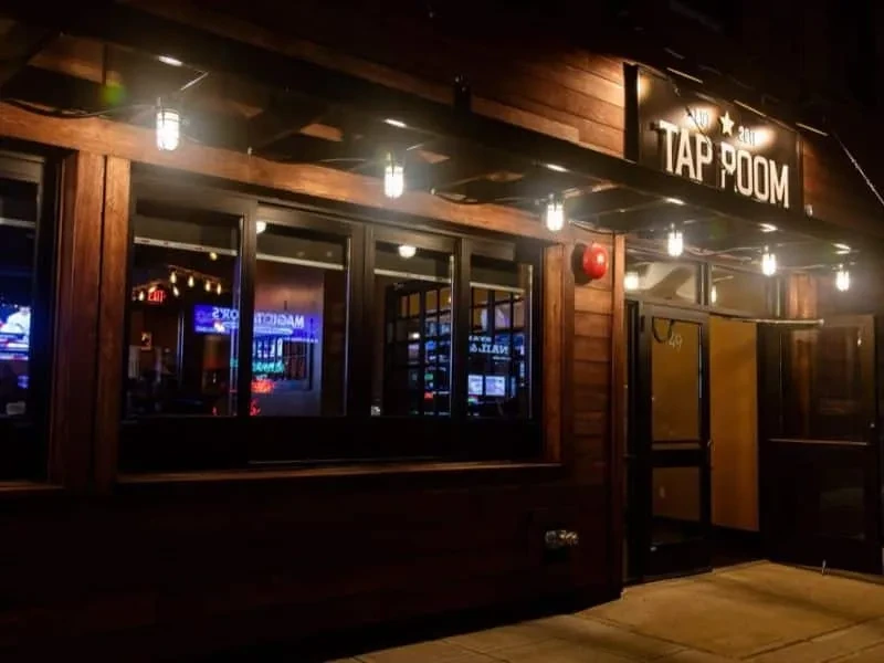 Dark wooden "TAP ROOM" facade illuminated by string lights at night.