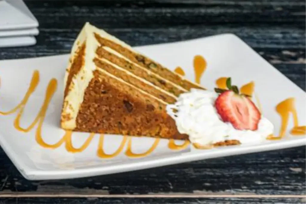 Slice of carrot cake with whipped cream, strawberry, and caramel drizzle.