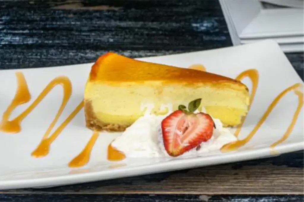 Slice of cheesecake with strawberry, whipped cream, and caramel drizzle.