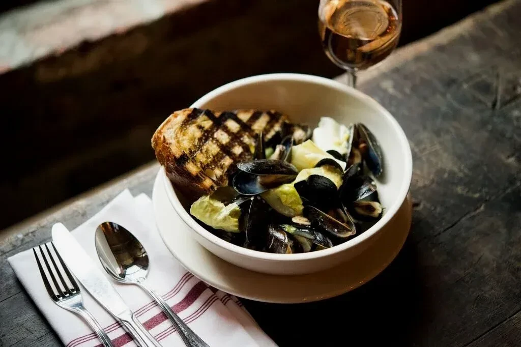 A bowl of mussels and grilled bread on a wooden table.