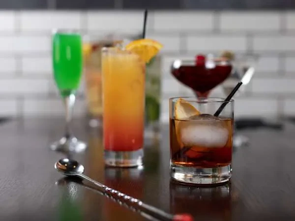 Various colorful cocktails with a bar spoon on a dark counter.