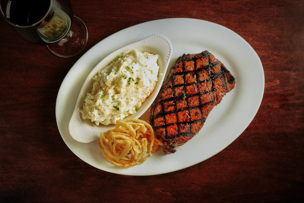 Grilled steak, mashed potatoes, and onion rings on a white plate.