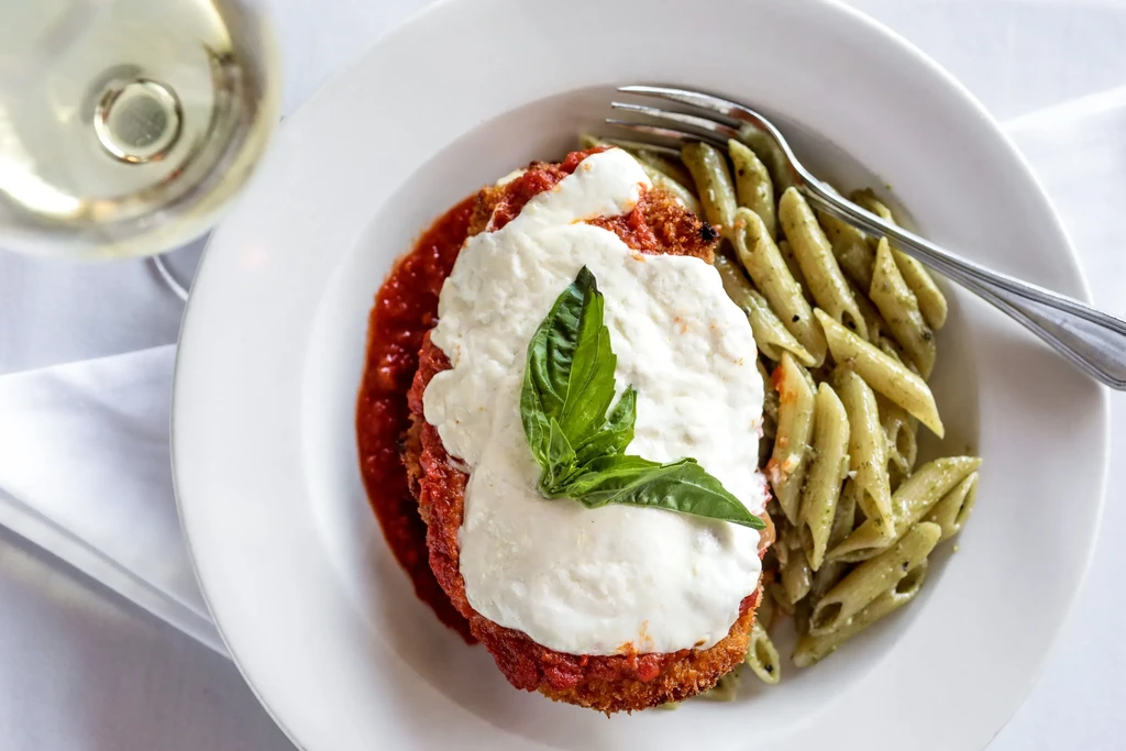Overhead shot of chicken parmesan, pesto pasta, and white wine.