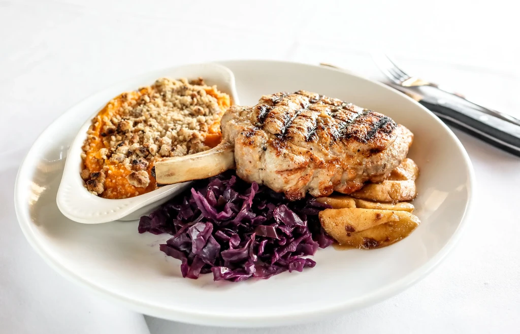 Grilled pork chop with sweet potato casserole, red cabbage, and apple slices.