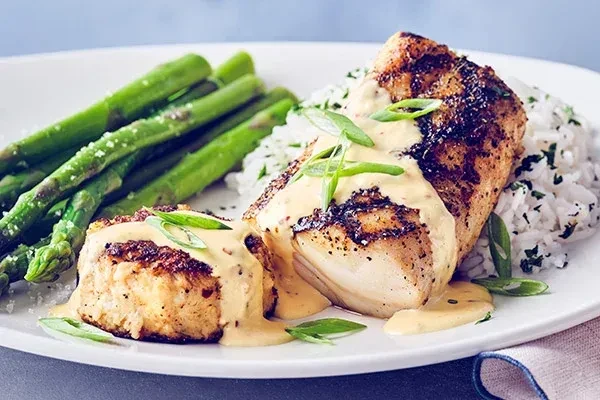 Golden grilled fish or chicken with creamy sauce, rice, and asparagus.