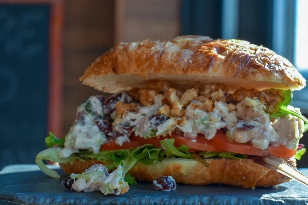 A croissant sandwich with chicken salad, cranberries, lettuce, and tomato.