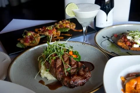 Grilled steak with mashed potatoes, appetizers, and a cocktail on a table.