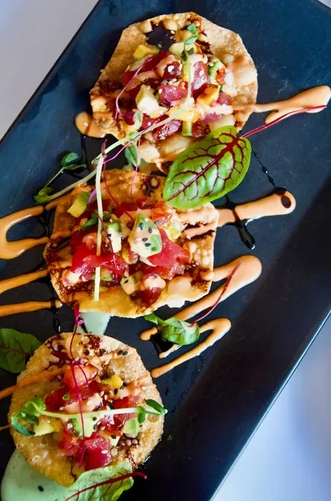 Three tuna and avocado tostadas on a black rectangular plate.