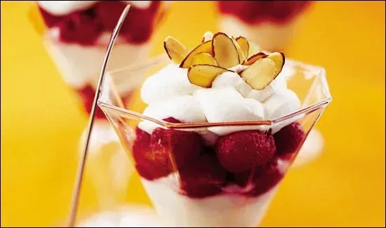 Raspberry and cream dessert in a clear glass with almond slivers.