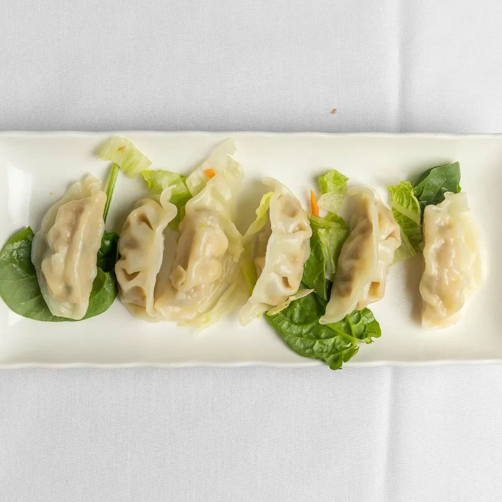 Steamed dumplings with spinach and lettuce on a white plate.
