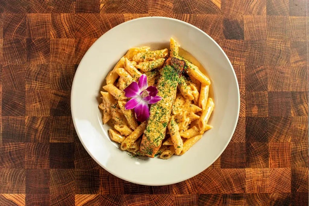 Plate of penne pasta with salmon, garnished with parsley and orchid.