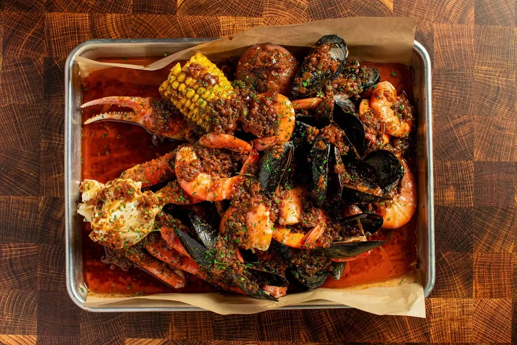A seafood boil with corn, crab, shrimp, and mussels on a metal tray.