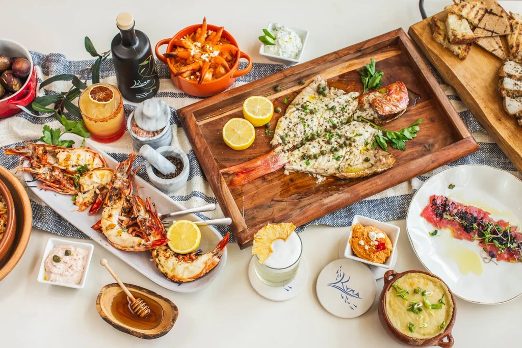A table full of Mediterranean seafood, appetizers, drinks, and various sauces.