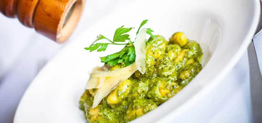 Gnocchi with pesto, parmesan, and parsley in a white bowl.