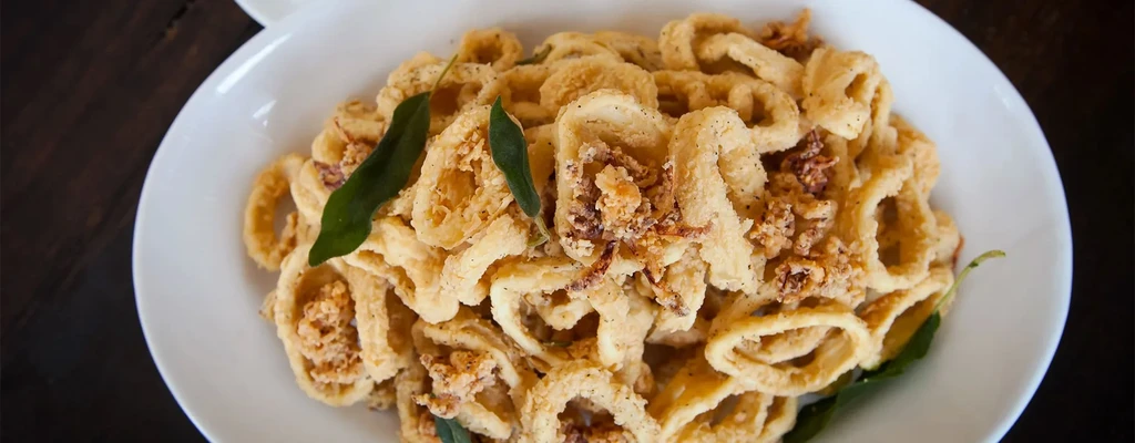 A white bowl overflowing with crispy fried calamari rings and green leaves.