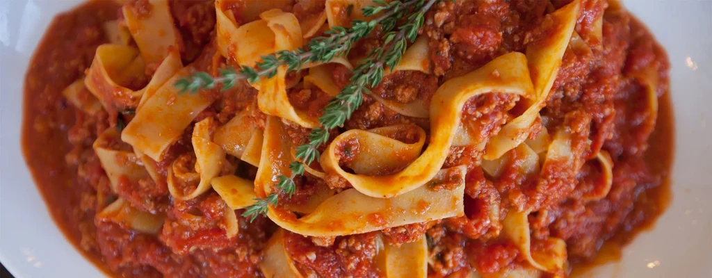Pasta with red sauce and sprig of thyme on white plate.