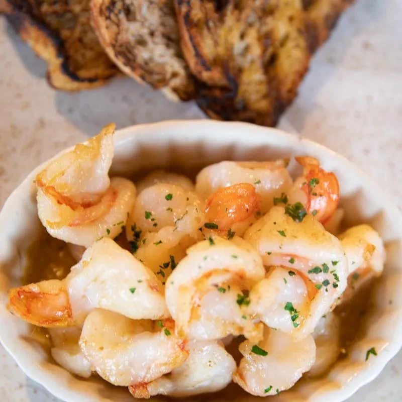 A bowl of shrimp garnished with parsley, with toasted bread in the background.