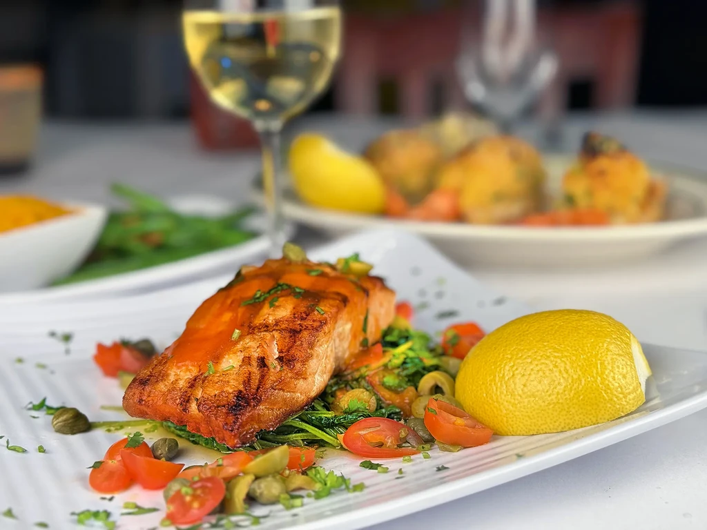 A close-up of a salmon fillet with vegetables and a lemon wedge.