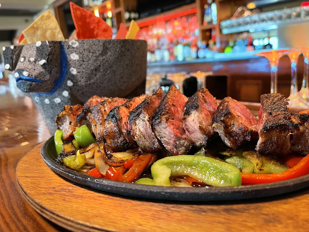 Sliced beef fajitas with peppers and onions on a sizzling platter.